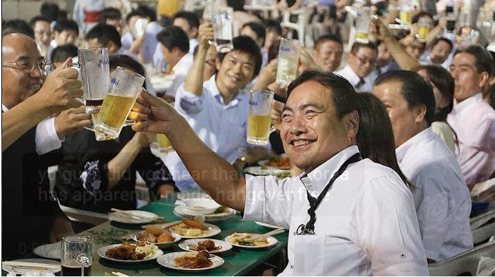 People eating and sitting at tables holding up cups of beer or alcohol